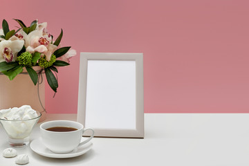 photo frame, orchid flowers, cup of tea and sweets on the pink background. empty space for text. mock up with copy space.
