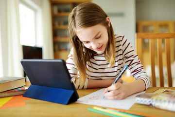 Smart preteen schoolgirl doing her homework with digital tablet at home. Education and distance...