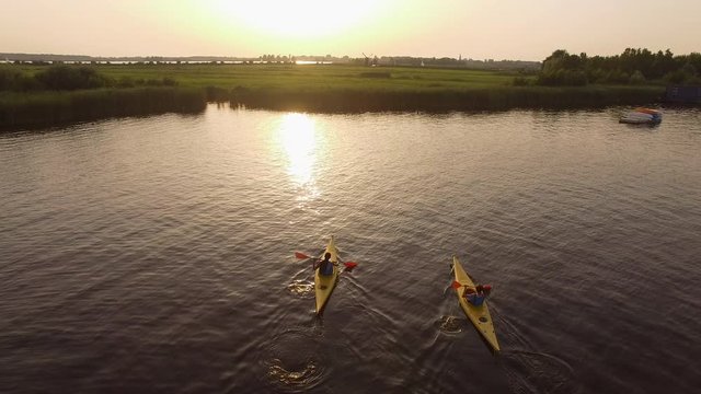 Cinematic drone shot of two people kayaking towards the sunset