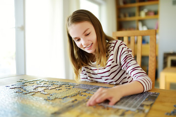 Cute young girl playing puzzles at home. Child connecting jigsaw puzzle pieces in a living room...
