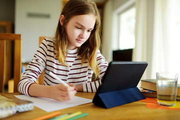 Smart preteen schoolgirl doing her homework with digital tablet at home. Education and distance learning for kids. Homeschooling during quarantine.