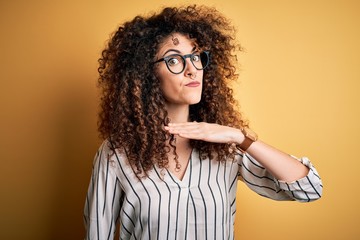 Young beautiful woman with curly hair and piercing wearing striped shirt and glasses cutting throat...