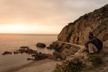 Seated man watching the sunrise on a beach in Ceuta