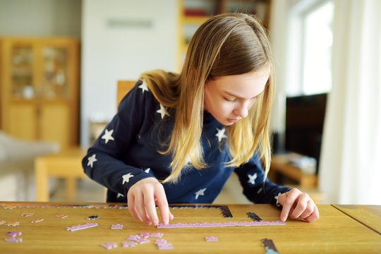 Cute Young Girl Playing Puzzles At Home. Child Connecting Jigsaw Puzzle Pieces In A Living Room Table. Kid Assembling A Jigsaw Puzzle. Fun Family Leisure.