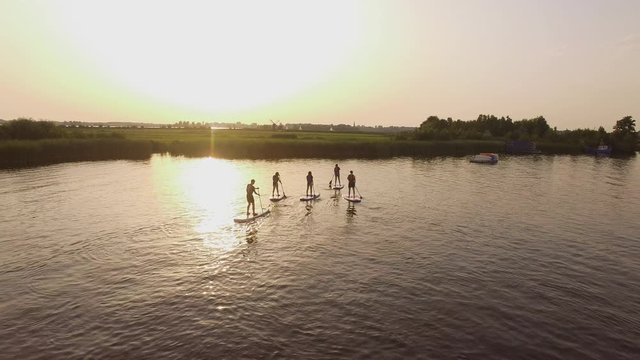 Cinematic drone shot of a group of stand up paddle boarders during a beautiful calm sunset