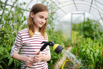Adorable young girl watering variuos vegetables in a greenhouse on sunny summer day. Gardening...