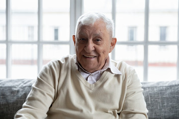 Head shot portrait positive old man feels healthy sitting on couch looking at camera. Healthcare and health exam check up for senior clinic advertisement, care about old people baby boomer generation