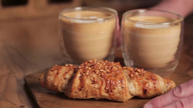 Waiter putting two cups of latte coffee and a croissant on a table. Restaurant street food lifestyle.