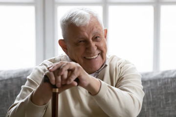 Physically disabled positive old grandfather seated on couch resting at home holding in palms...