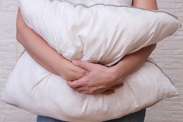 Woman holding white fluffy pillow in hands, hugging a pillow - sleeping and resting concept