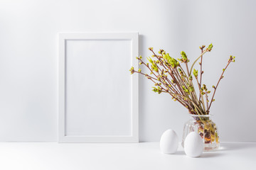 Home interior with easter decor. Mockup with a white frame and green buds on branches in a vase on a light background