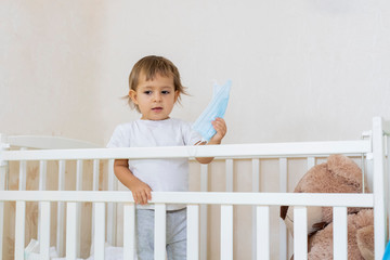 quarantine coronavirus covid-19 pandemic concept. a little cute serious baby is in a baby cot at home in safety and holding a medical mask. copy space