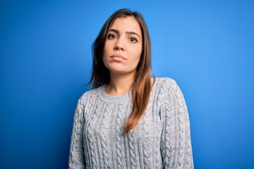Fototapeta premium Beautiful young woman wearing casual wool sweater standing over blue isolated background Relaxed with serious expression on face. Simple and natural looking at the camera.