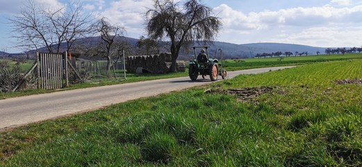 Ein Landwirt fährt auf einem Traktor auf einem Feldweg zu seinem Acker 
