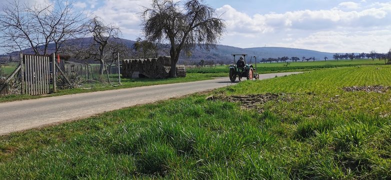 Ein Mann fährt auf einem Traktor über Feldweg 