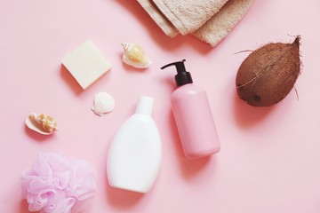Spa cosmetics with natural organic ingredients. Bath products with coconut oil. White shampoo bottle, nourishing hair balm, beige cotton towel, soap bar and sponge on a pink background - obrazy, fototapety, plakaty