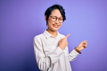 Young beautiful asian girl wearing casual shirt and glasses standing over purple background...