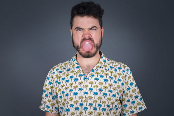 Fototapeta premium Body language. Disgusted stressed out pretty man posing against gray wall, frowning his face, demonstrating aversion to something.