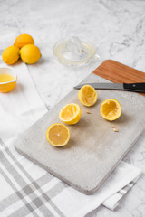Whole and Cut Lemons on Cement Cutting Board on White Marble Counter; Lemon Juicer Nearby with Cup of Lemon Juice