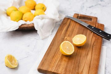 Fresh Lemons in a Wooden Bowl on a White Marble Countertop; One Cut in Half on Wooden Cutting Board