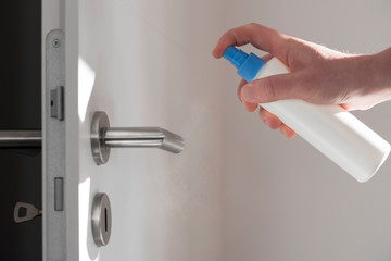 Hand with disinfektion spray spraying a door handle
