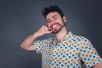 Fototapeta premium Attractive young male in casual clothes imitates telephone conversation, keeps hand near ear as if holding mobile phone, has confident facial expression, isolated outdoors. Call me!