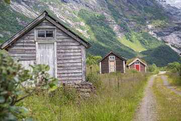 Fototapeta na wymiar Abandoned village with different colored wooden houses in an idyllic location, between mountains, glacier in the background, abundant green vegetation on a summer day in Norway