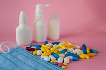 concept of treatment and protection against viruses. Multi-colored pills and a protective mask on a pink background.Spray and antiseptics in the background, selective focus.