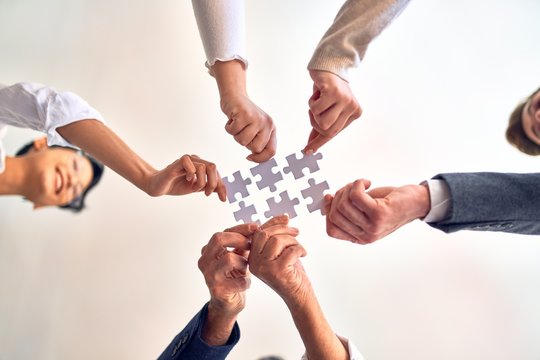 Group of business workers with hands together connecting pieces of puzzle at the office