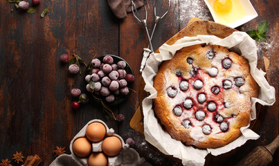 Bakery products. Biscuit cake with cherries and powdered sugar. Eggs, flour, cinnamon, star anise, mint and rolling pin on a dark old wooden background. Background image, copy space