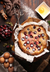 Bakery products. Biscuit cake with cherries and powdered sugar. Eggs, flour, cinnamon, star anise, mint and rolling pin on a dark old wooden background. Background image, copy space