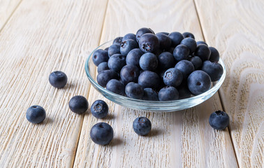 Sweet ripe blueberries or Vaccinium myrtillus in a glass bowl on a white rustic wooden table. Fruits and vegetables, vegetarian and healthy eating.