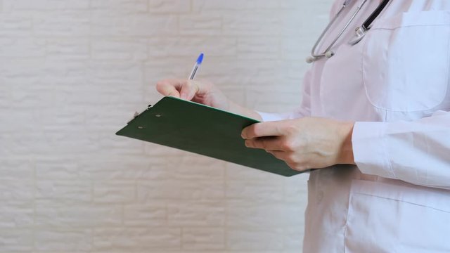 Unrecognizable female woman doctor writing a diagnosis, case medical history on a prescription board