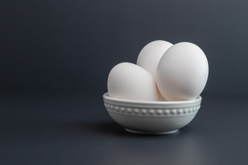 Eggs Sitting in white bowl isolated on studio black background three large eggs from grocery store.