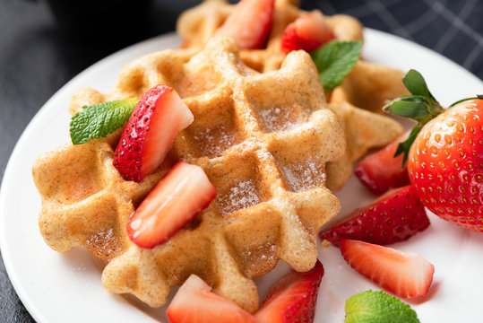 Belgian waffles with strawberries on white plate closeup view