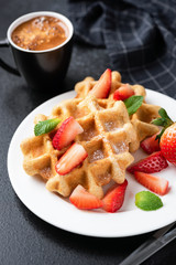 Belgian waffles with strawberries and sugar and cup of espresso coffee on black background