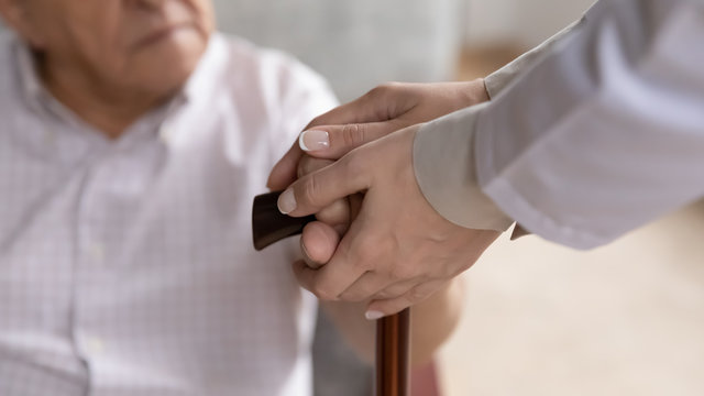 Caring female nurse hands holding old man patient arms touch walking stick close up image. Provide help to older generation person, psychological physical support, physiotherapy, nursing home concept