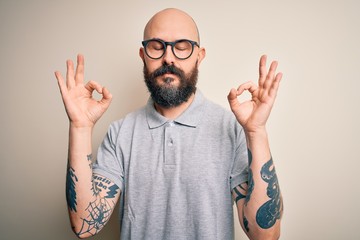 Handsome bald man with beard and tattoo wearing casual polo and glasses relax and smiling with eyes closed doing meditation gesture with fingers. Yoga concept.