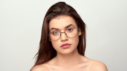 beautiful young girl with brown hair in fashionable glasses posing on a white background with bare shoulders, empty space for text