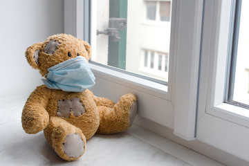 Sick teddy bear in home quarantine wearing a medical mask against viruses during coronavirus and flu outbreak.