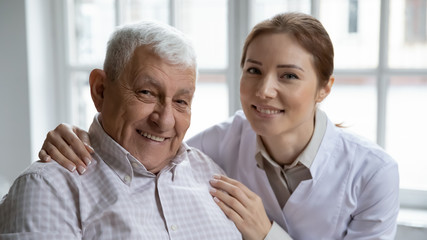 Young nurse in white coat hugging old 80s man smiling looking at camera. Portrait of satisfied patient and his caregiver. Medical care of older generation people, geriatrics medicine, nursing concept