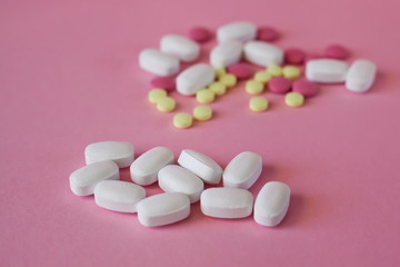 White oval-shaped tablets, antibiotics on the background of other multi-colored tablets, selective focus on a pink background.