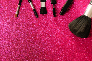 Makeup brush and decorative cosmetics on a pink background.