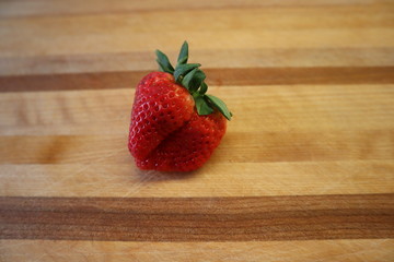 Une fraise imparfaite sur un plateau de bois