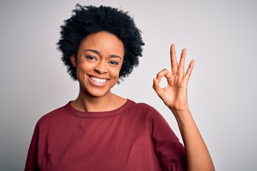 Young beautiful African American afro woman with curly hair wearing casual t-shirt standing smiling positive doing ok sign with hand and fingers. Successful expression.