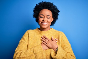 Young beautiful African American afro woman with curly hair wearing yellow casual sweater smiling...