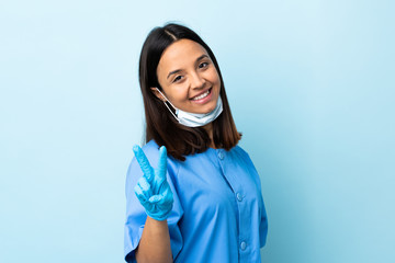 Surgeon woman over isolated blue background smiling and showing victory sign