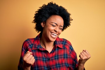 Fototapeta na wymiar Young beautiful African American afro woman with curly hair wearing casual shirt very happy and excited doing winner gesture with arms raised, smiling and screaming for success. Celebration concept.