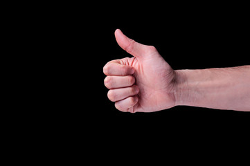 Hand of european human shows thumb signal, usually described as a thumbs-up sign on isolated black background