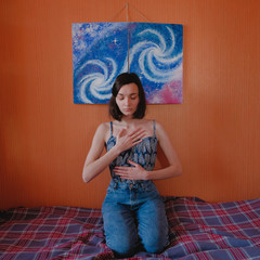 Young woman sitting on bed under galaxy painting and practicing yoga. Home meditation concept
